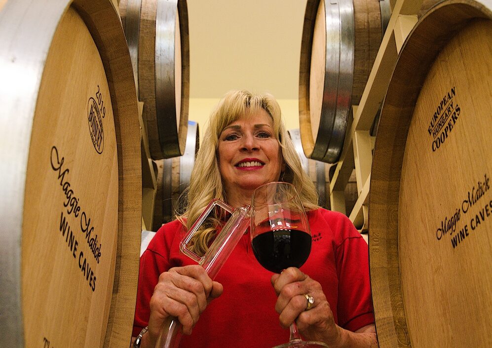 Maggie Malick in the racks of barrels holding a wine thief